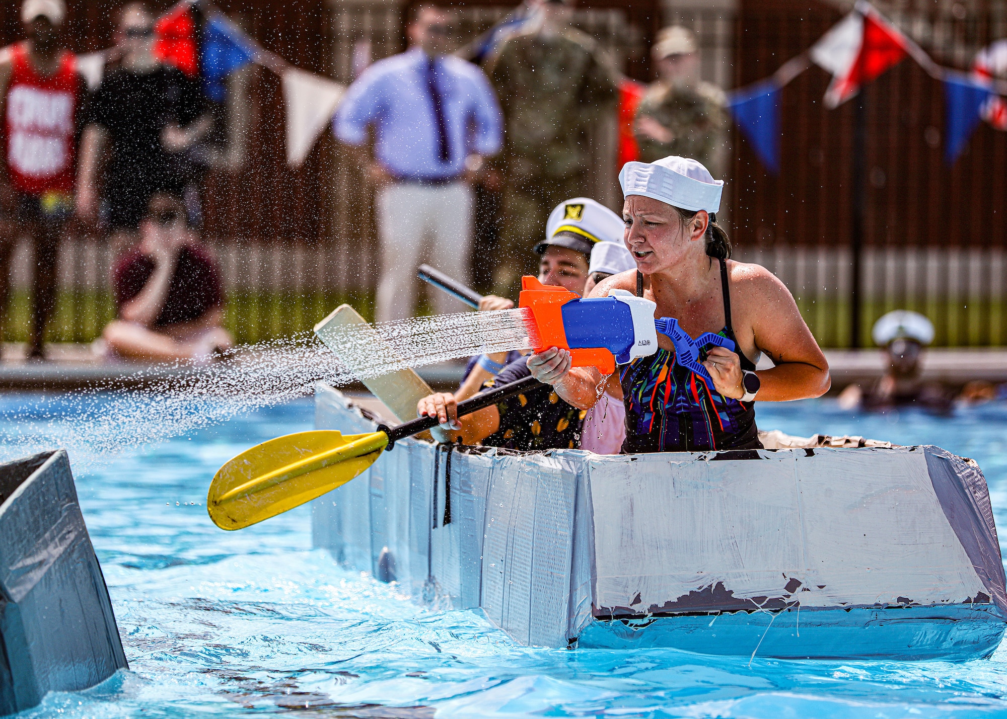 Senior Airman Stephanie Gillespie, front, 445th Maintenance Squadron fabrication flight non-destructive inspection technician, shoots water at another boat as her fellow squadron teammates, Staff Sgt. Lawrence Depasquale, middle, and Master Sgt. Bradley Swindall, back, both 445th MXS aircraft structural maintenance mechanics, paddle during the Wright-Patterson Air Force Base Cardboard Boat Regatta held on base at Patterson Pool June 30, 2023. The 445th MXS team made their boat, Ship for Brains, out of cardboard, glue and tape. They won “The Packed Pontoon Award” for most people on a boat. Additionally, they won the “Soggy Bottom Award” for having the last boat standing during the battle royal in which the participants attempt to sink each other’s boats by ramming or filling with water by use of water guns or buckets. Ten teams participated in the event this year with more than 100 people in attendance.