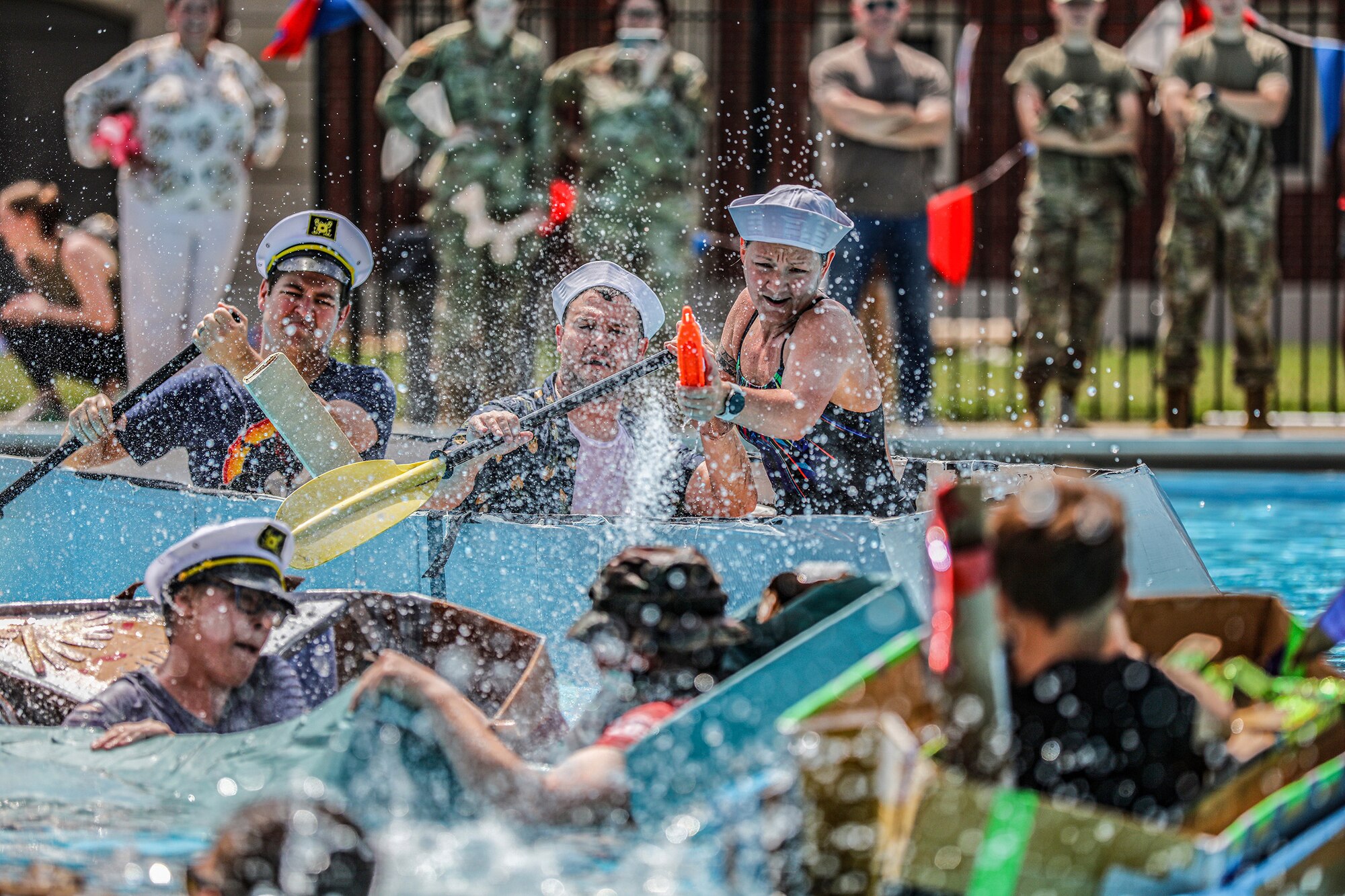 Senior Airman Stephanie Gillespie, right, 445th Maintenance Squadron fabrication flight non-destructive inspection technician, Staff Sgt. Lawrence Depasquale, middle, and Master Sgt. Bradley Swindall, left, both 445th MXS aircraft structural maintenance mechanics, compete in the Wright-Patterson Air Force Base Cardboard Boat Regatta held on base at Patterson Pool June 30, 2023. The 445th MXS team made their boat, Ship for Brains, out of cardboard, glue and tape. They won “The Packed Pontoon Award” for most people on a boat. Additionally, they won the “Soggy Bottom Award” for having the last boat standing during the battle royal in which the participants attempt to sink each other’s boats by ramming or filling with water by use of water guns or buckets. Ten teams participated in the event this year with more than 100 people in attendance.
