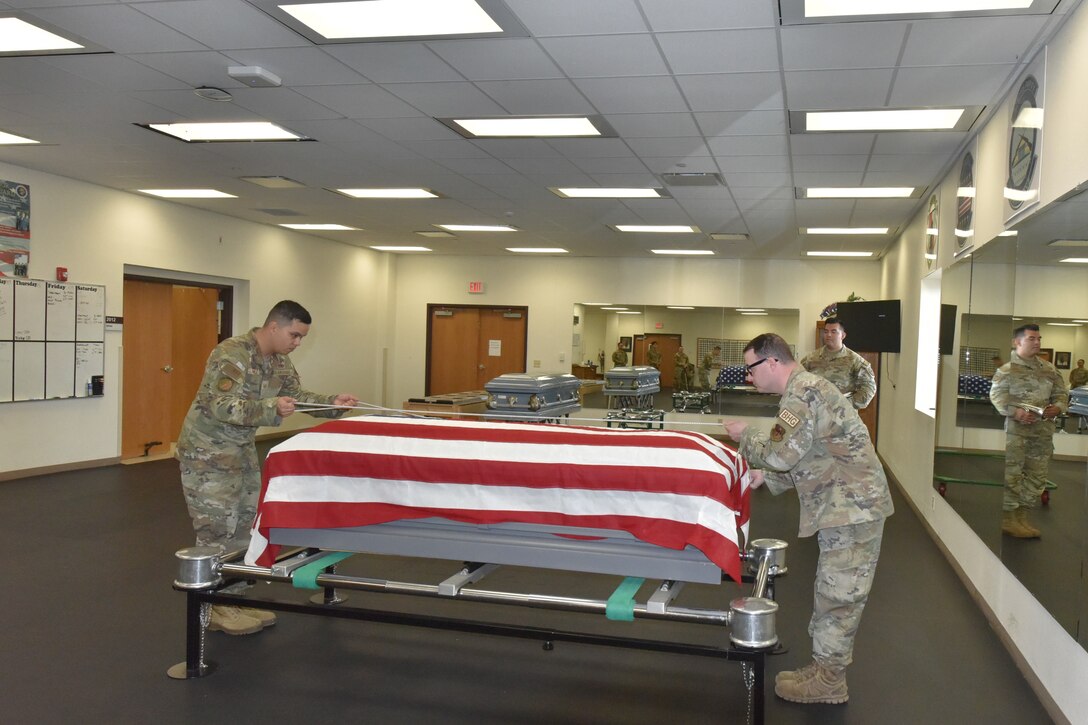 Two Airmen lean over a flag-draped coffin in their training area.