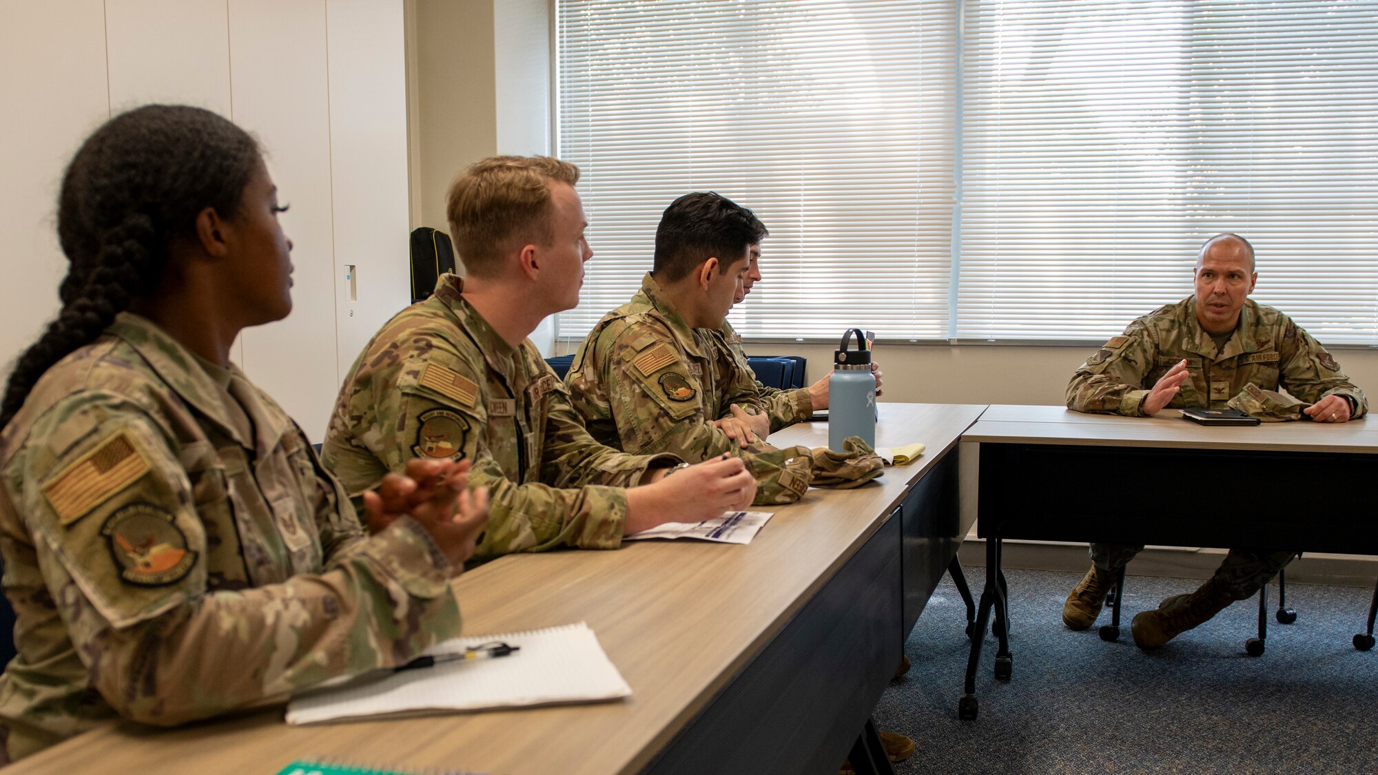 Three soldiers seated to the left of a commander look at the commander as he speaks