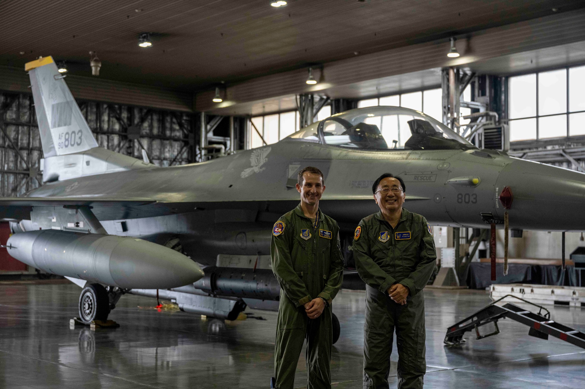 Two people pose in front of a fighter jet inside a hangar at Misawa Air Base.