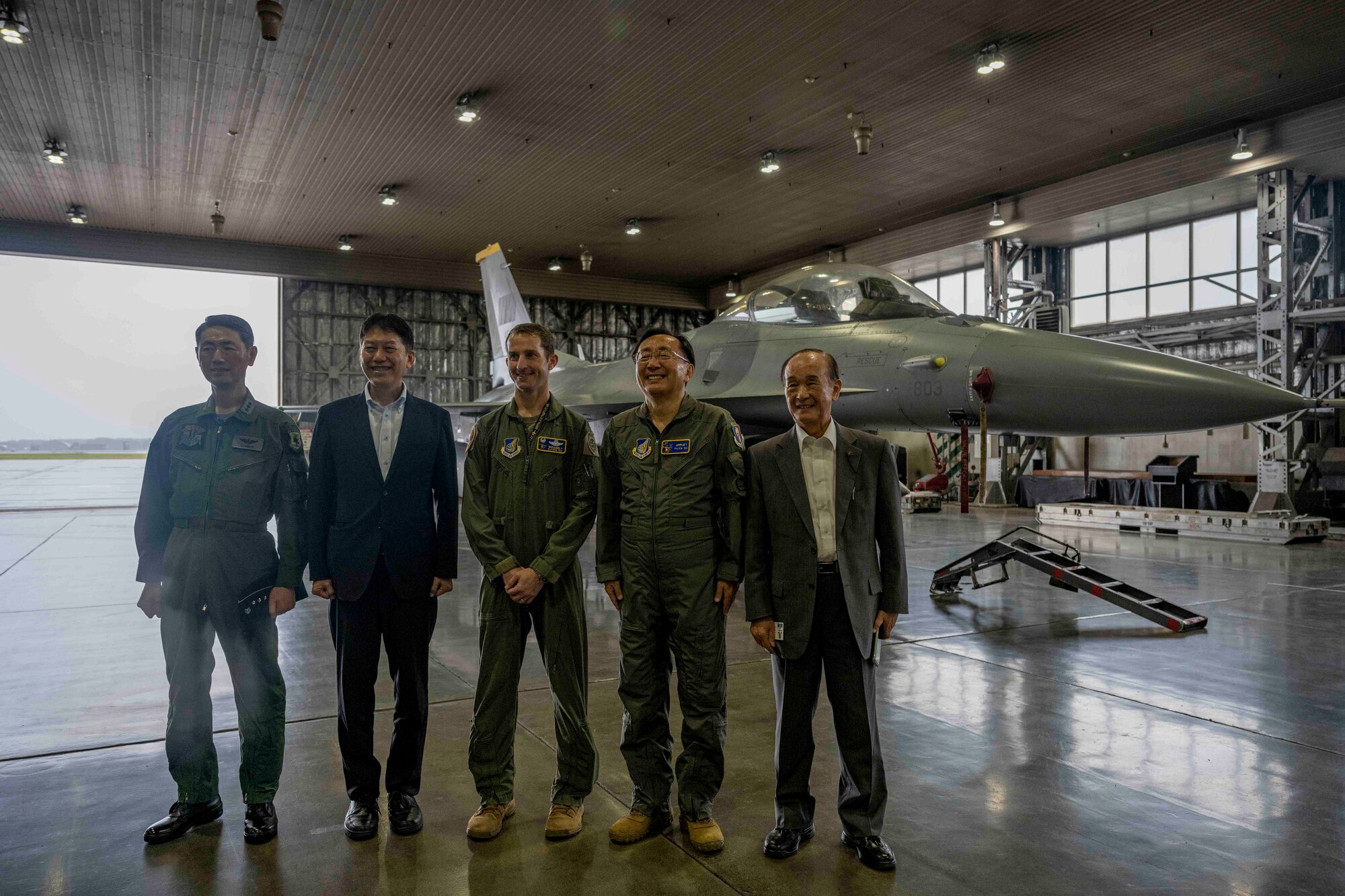 A group of people pose for a photo with a fighter jet in the background at Misawa Air Base.
