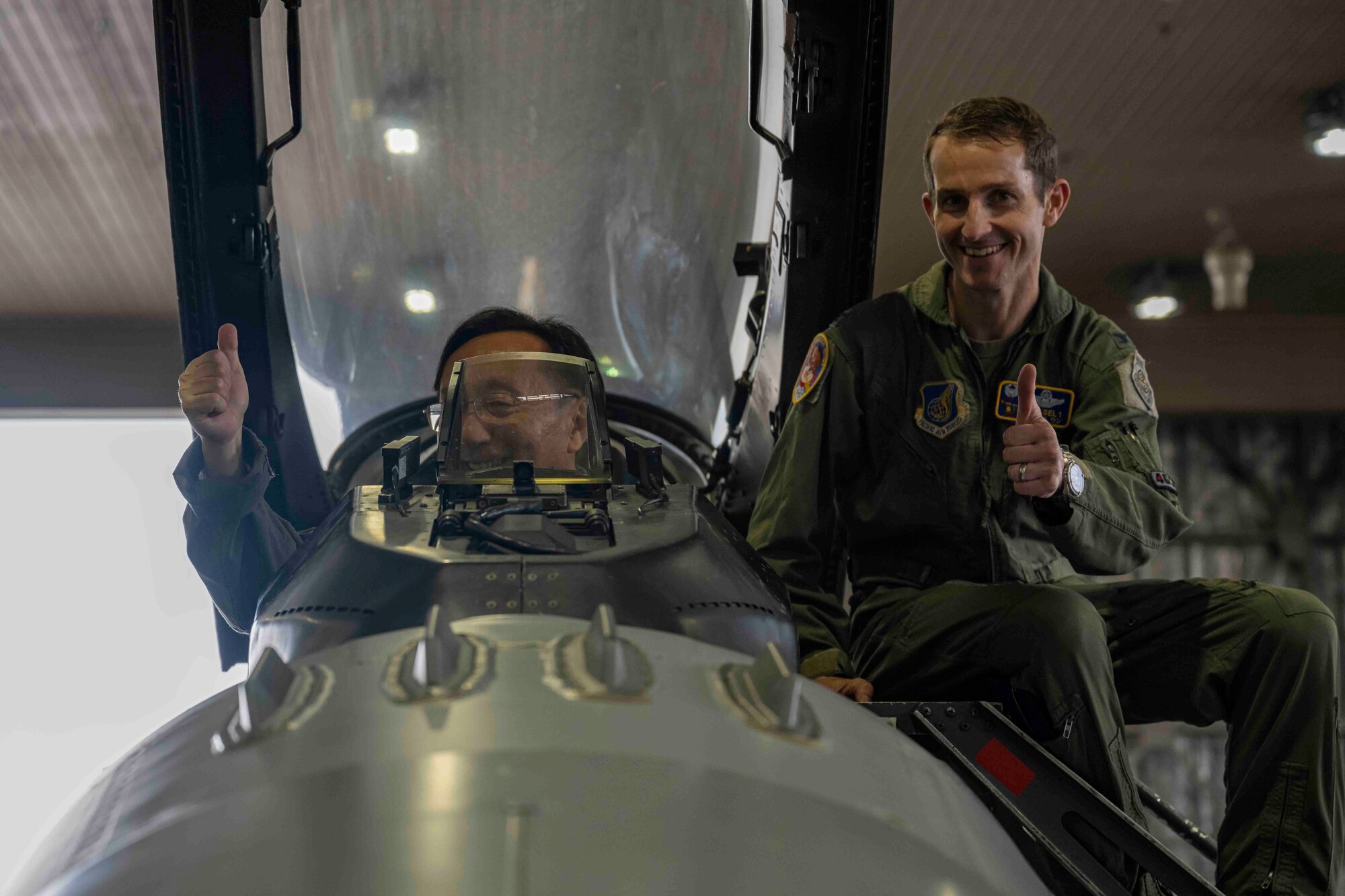 Two men give a thumbs up as they look inside the cockpit of a fighter jet in a hangar at Misawa Air Base.