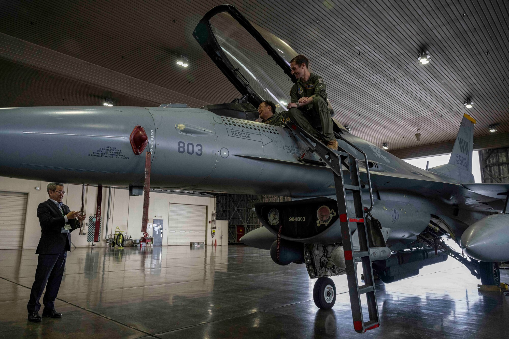 Two men look inside the cockpit of a fighter jet in a hangar at Misawa Air Base.