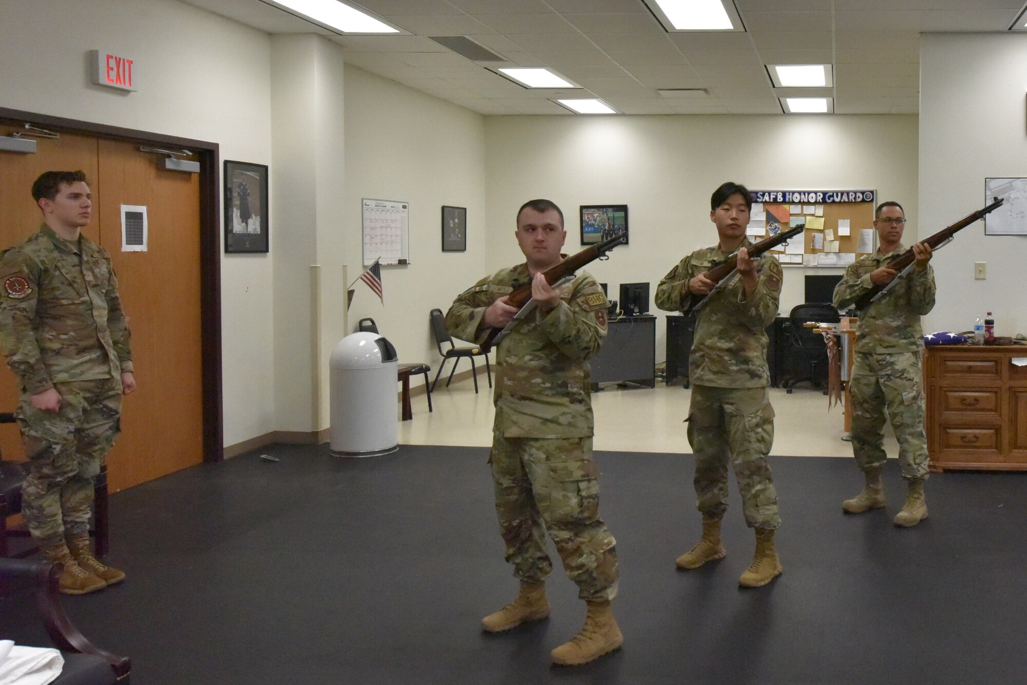 Three Airmen with ceremonial rifles dry fire while another airman stands at attention