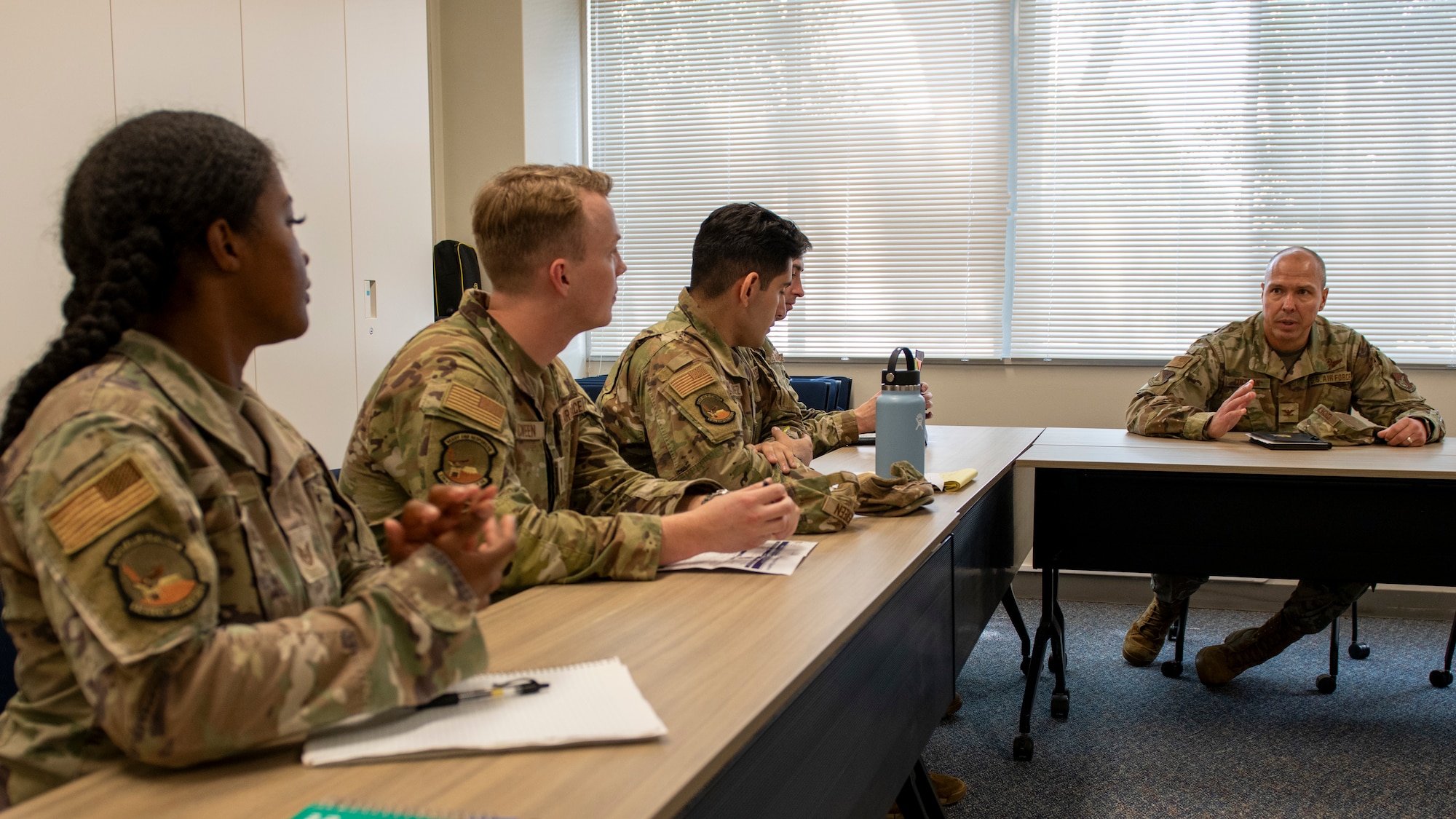 Three soldiers seated to the left of a commander look at the commander as he speaks