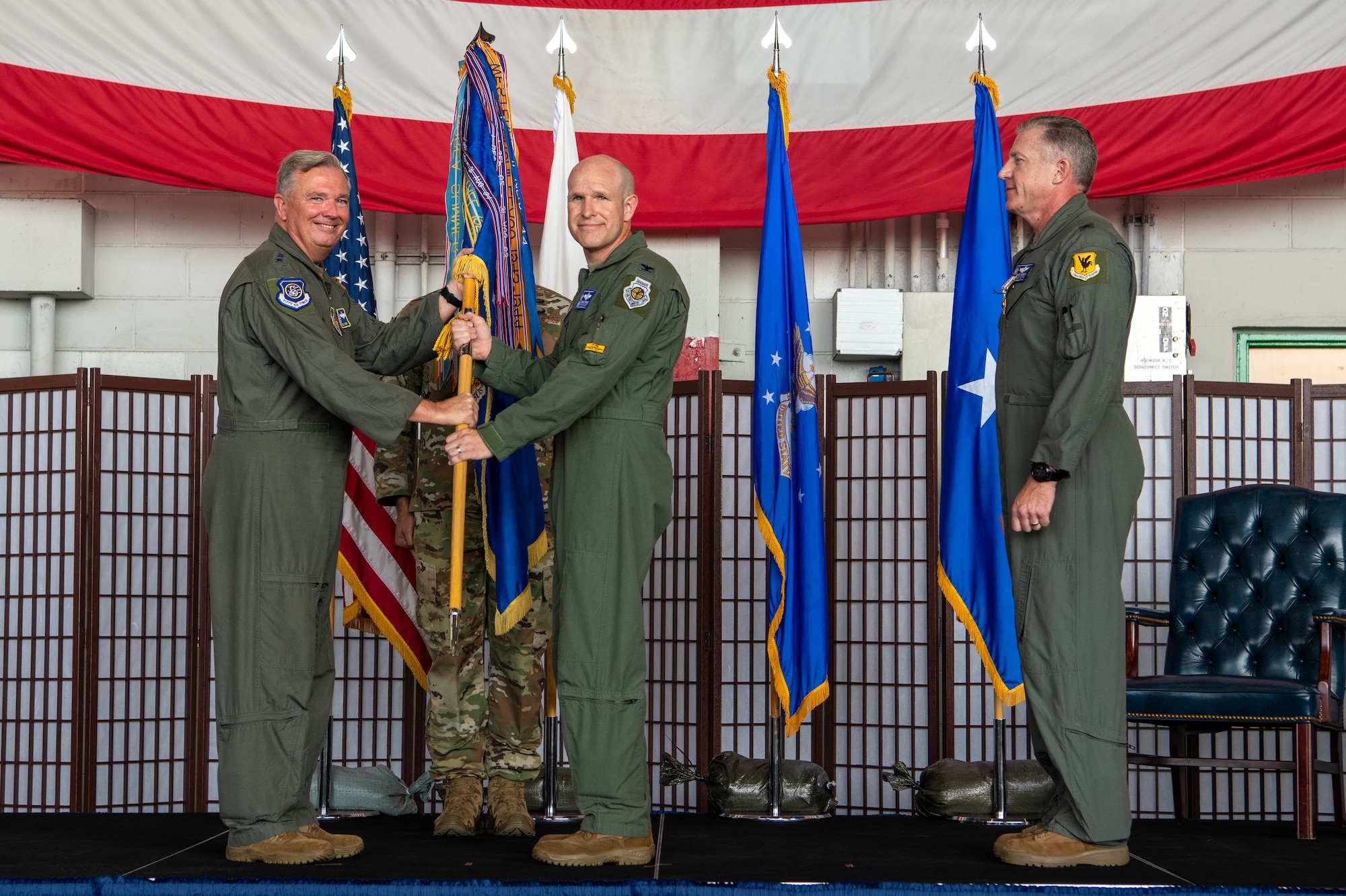 Four men stand on a stage while two hold a guidon staff.