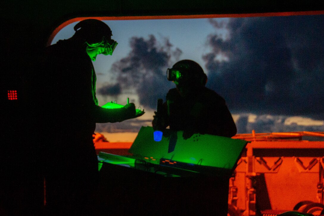 Two sailors inspect weapons at night.