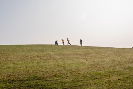 Sailors run atop a grass hill
