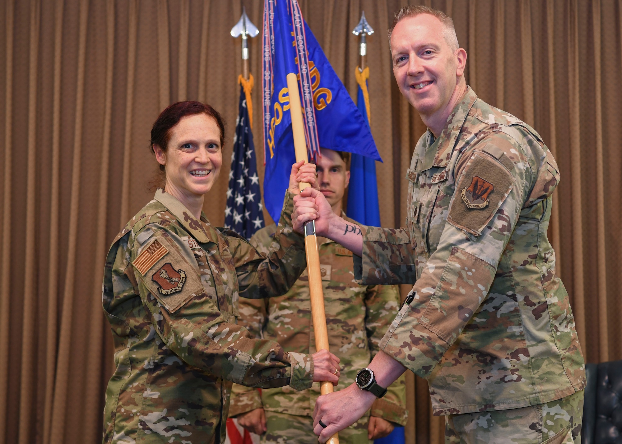 Two people in green uniforms hold a flag.