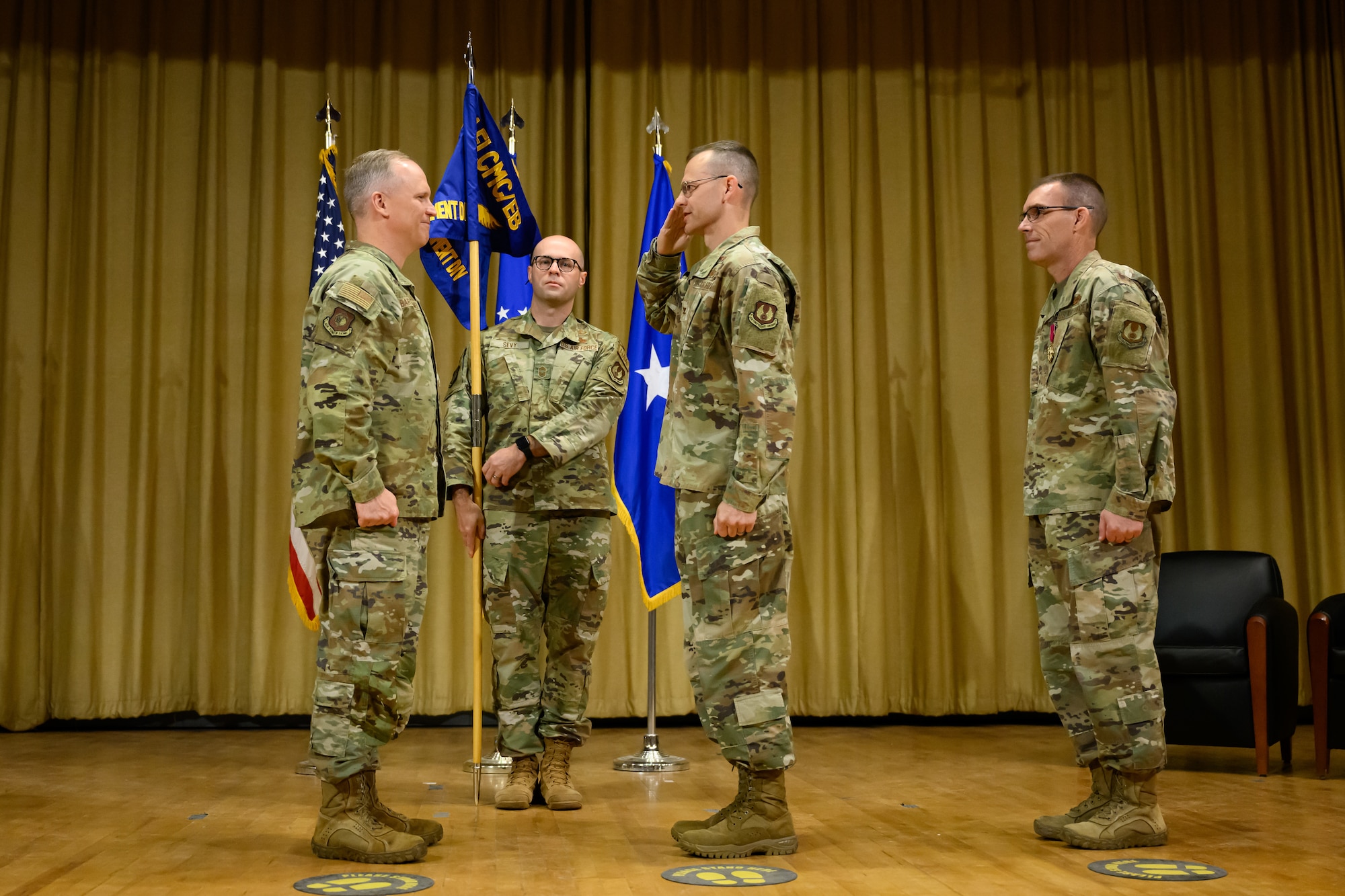 Col. Kendall Okeson at center salutes Brig. Gen. Jason Bartolomei at left while the guidon bearer and outgoing director watch the interaction.
