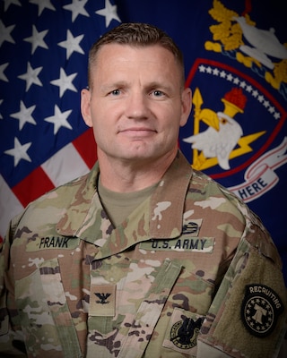 Male Army Soldier wearing ACUs posed in front of two flags.