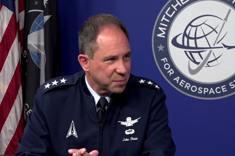 A man in a military uniform sits with his hands clasped in front of him.