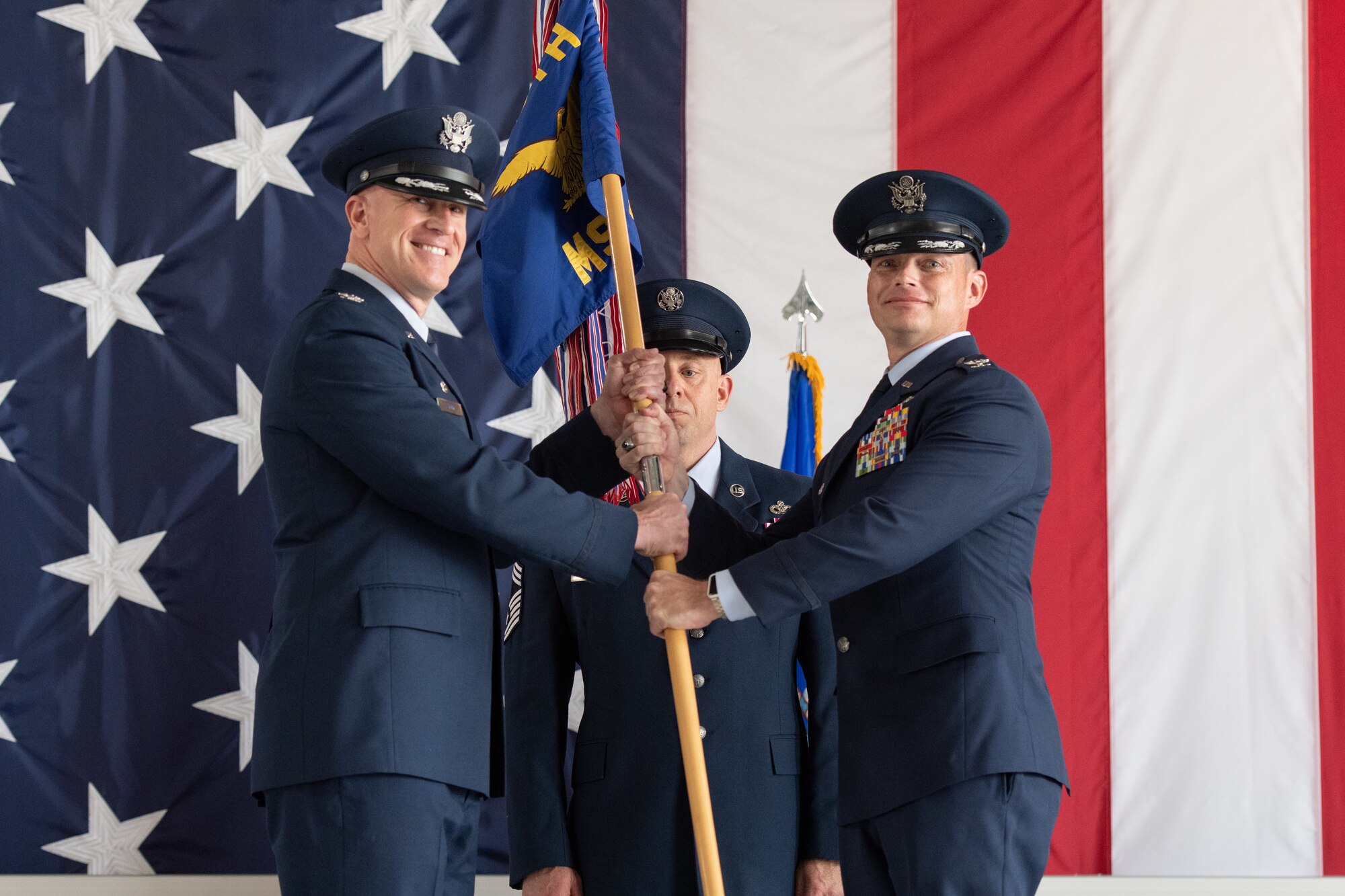 Uniformed man hands blue and yellow guidon to another uniformed man