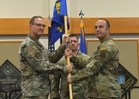 Colonel Kenneth Benton and Major Justin Cassidy pose holding a blue flag with gold letters as Major Cassidy takes command of 341st Munitions Squadron.