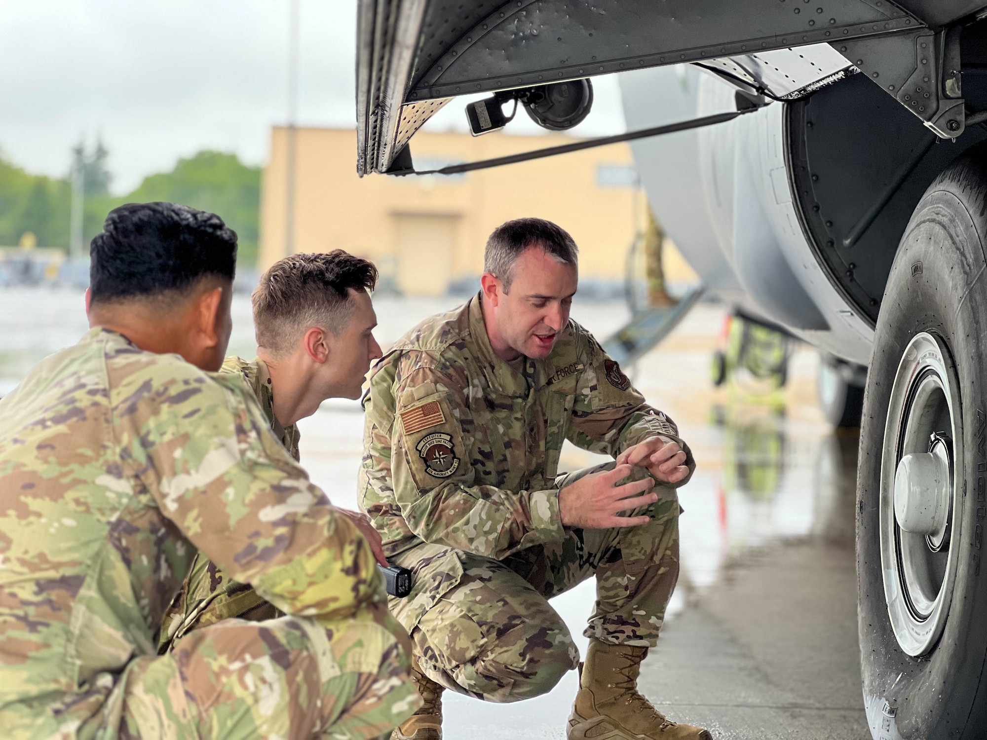 Three service members discuss the intricacies of the main landing gear of a transient MC-130J Commando II.