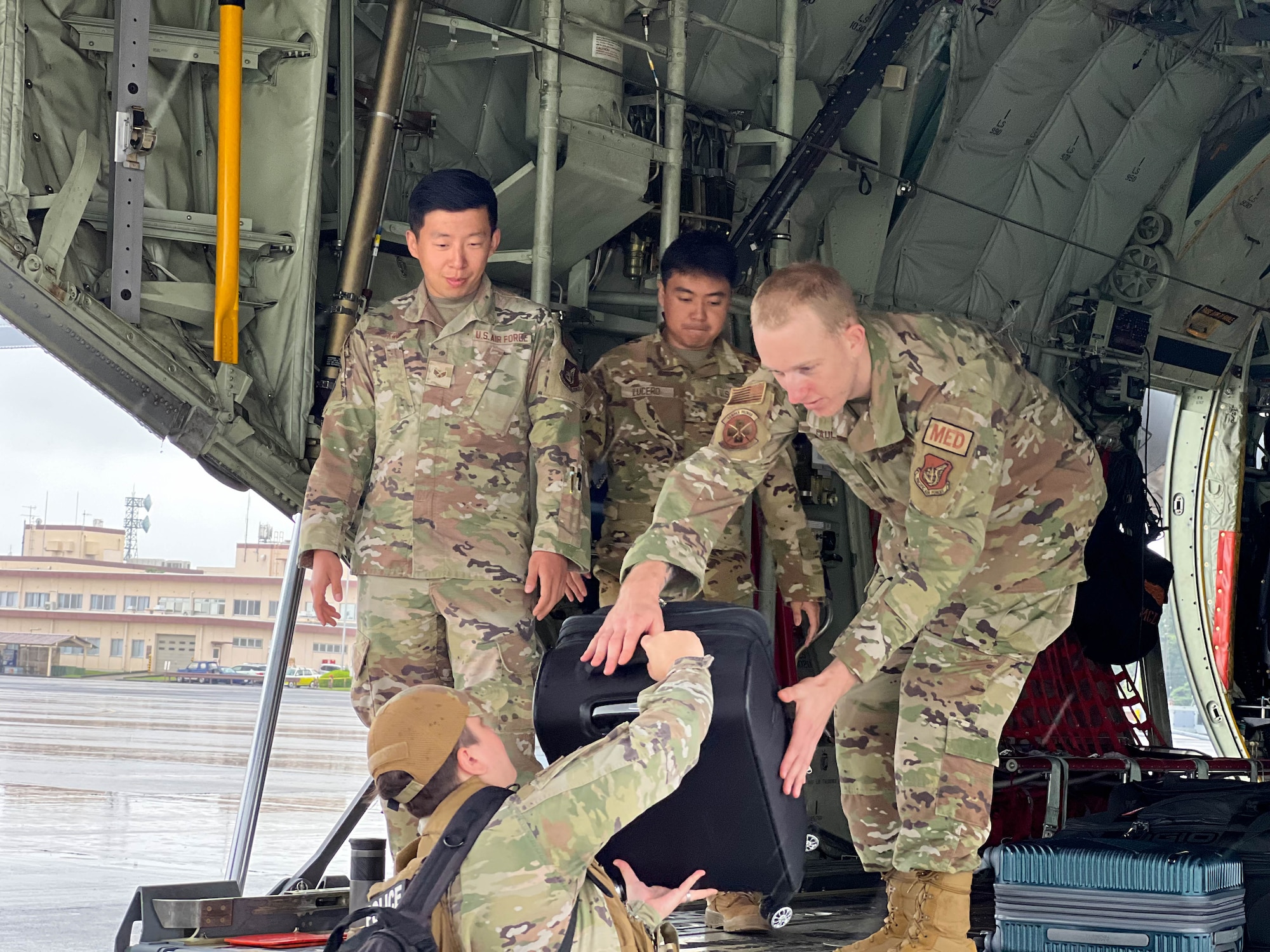 Two service members assist other service members in loading their equipment into a C-130J Super Hercules.