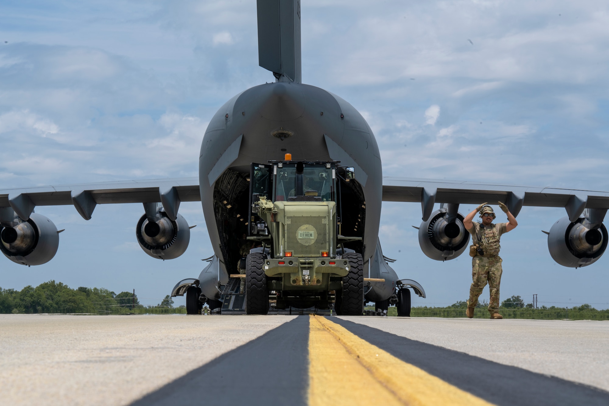 U.S. Air Force Staff Sgt. Andres Martinez, right, a 621st Mobility Support Operations Squadron enlisted air/ground liaison element (EAGLE) team member, marshals oncoming vehicles to load onto a C-17 Globemaster aircraft during Exercise SWAMP AVENGER at North Field, South Carolina, May 25, 2023.