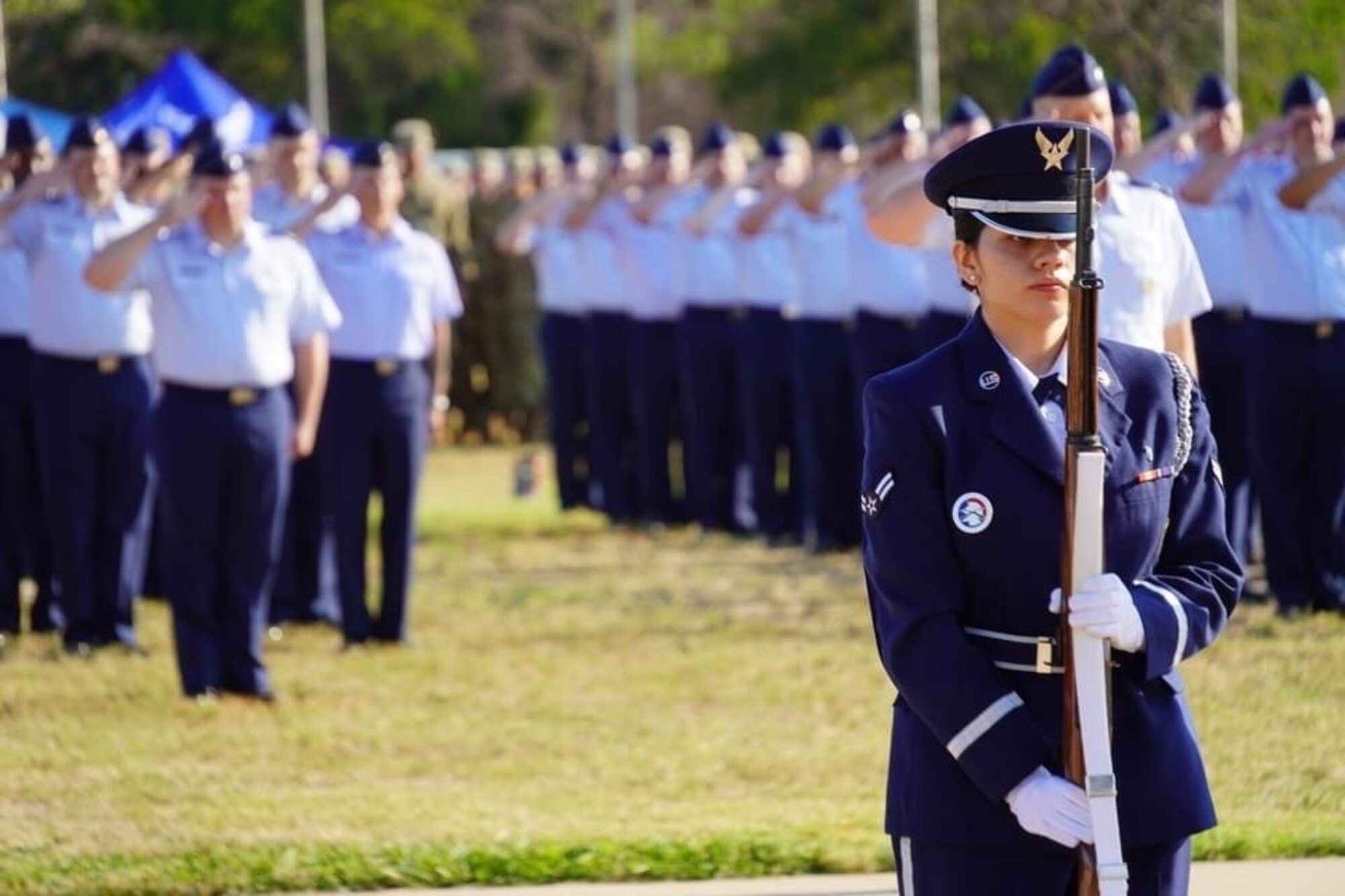 An Honor Guard member stands at attention with Airmen in the background.