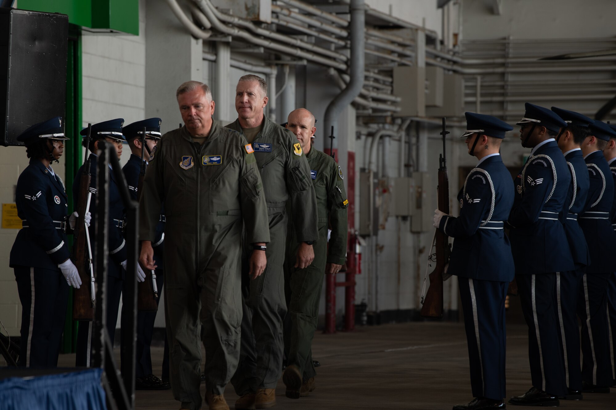 Three men walk towards a stage through a row of airmen.