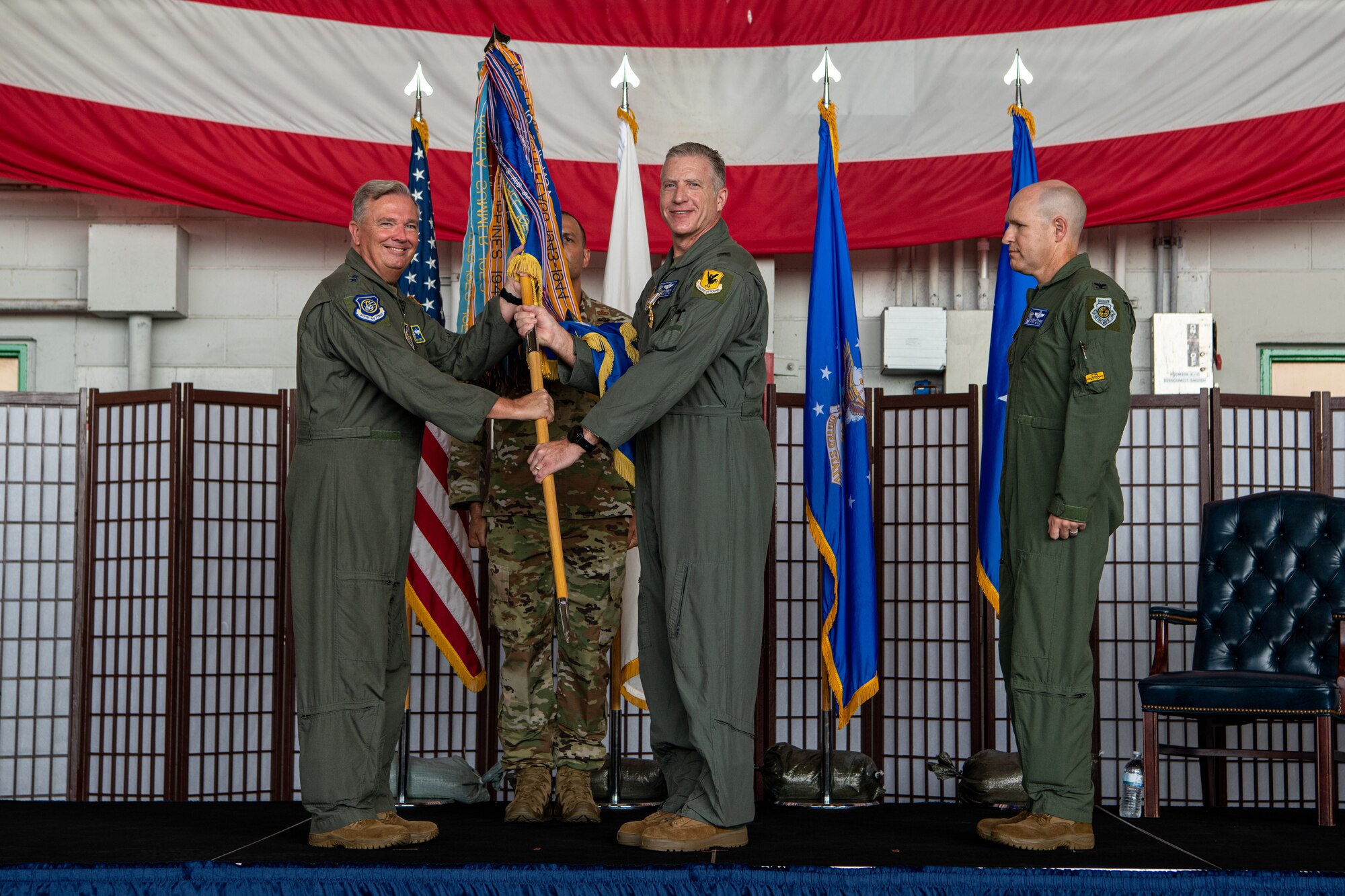 Four men stand on a stage while two men hold a guidon staff.