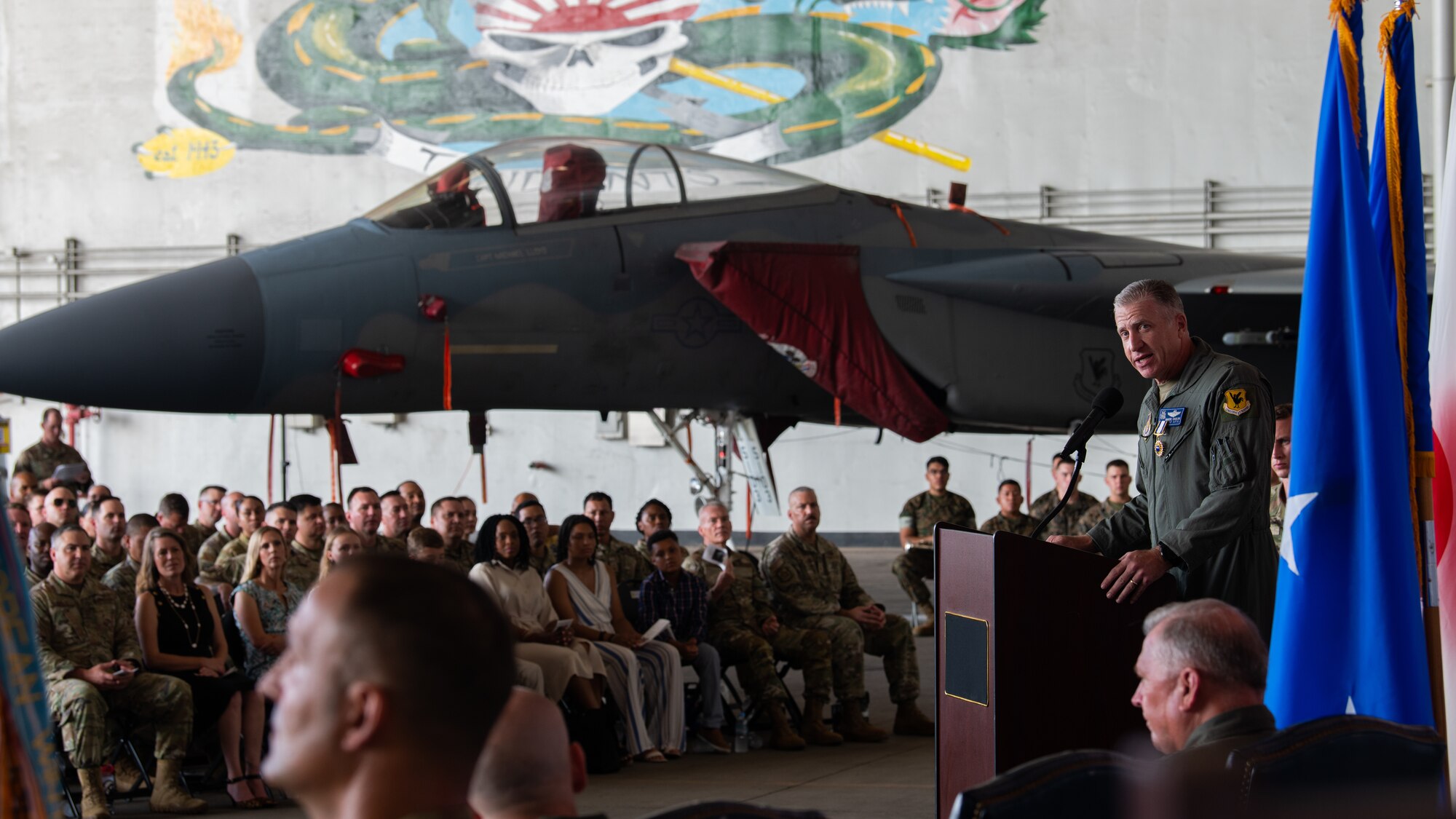 Man speaks to a crowd with a plane in the background.