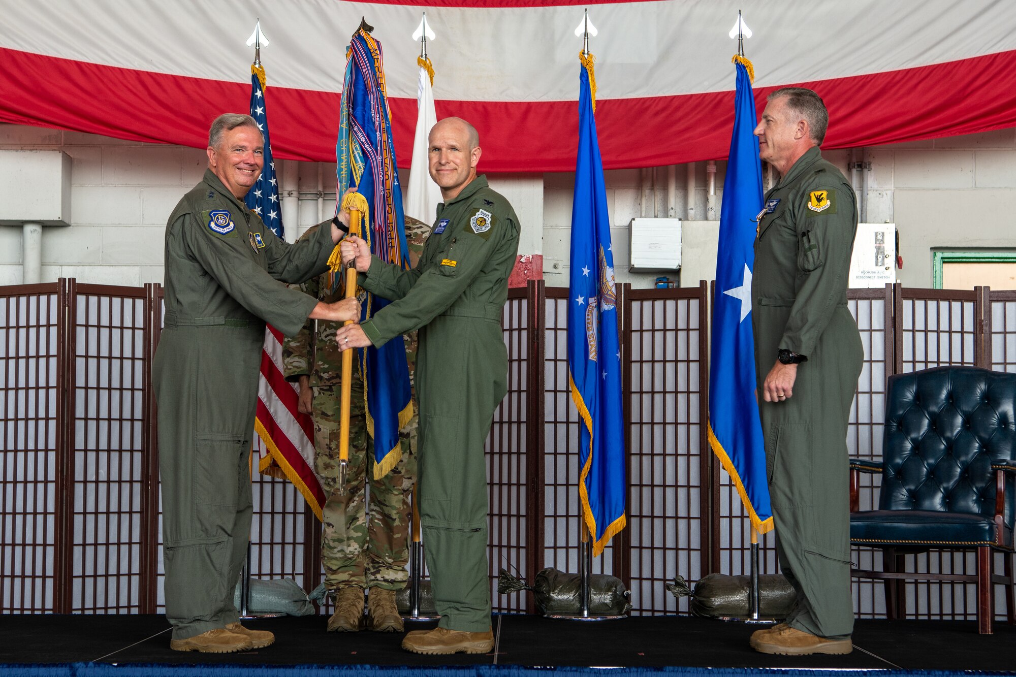 Four men stand on a stage while two hold a guidon staff.