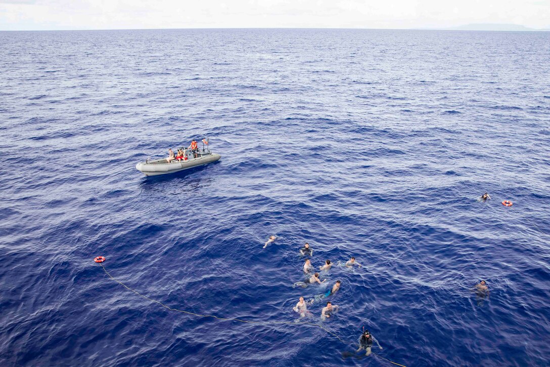 Sailors take a swim in the ocean as a rubber raft floats nearby.