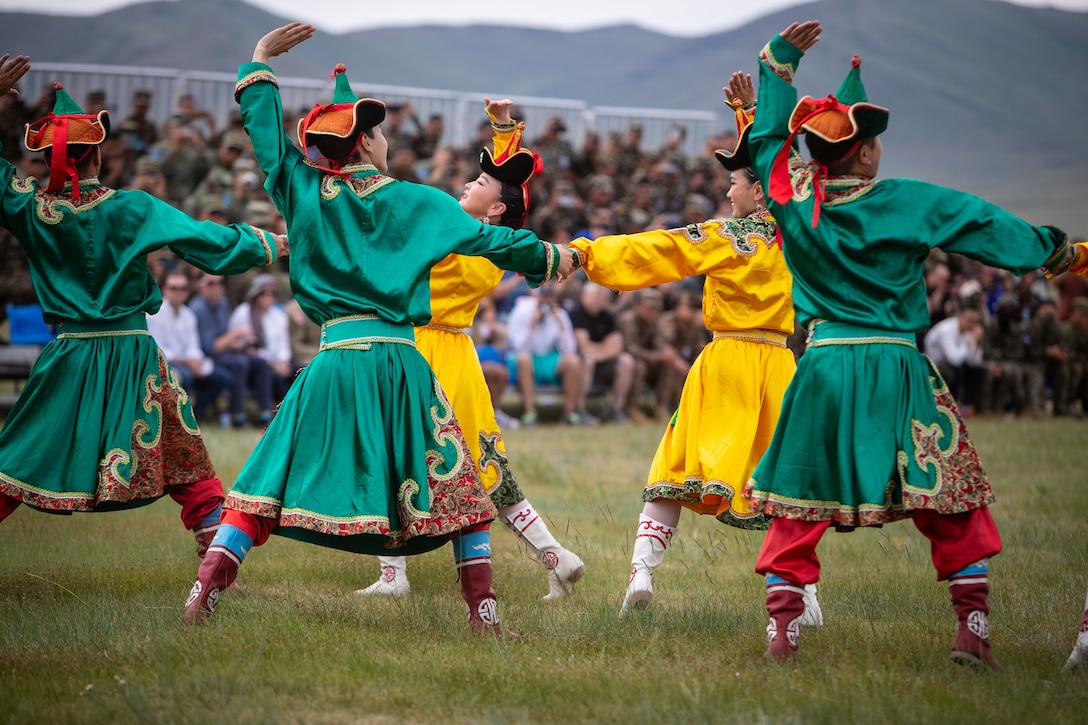 Mongolian dancers perform in a field as service members watch from the stands.