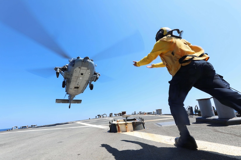 A sailor directs a helicopter on the deck of a ship.