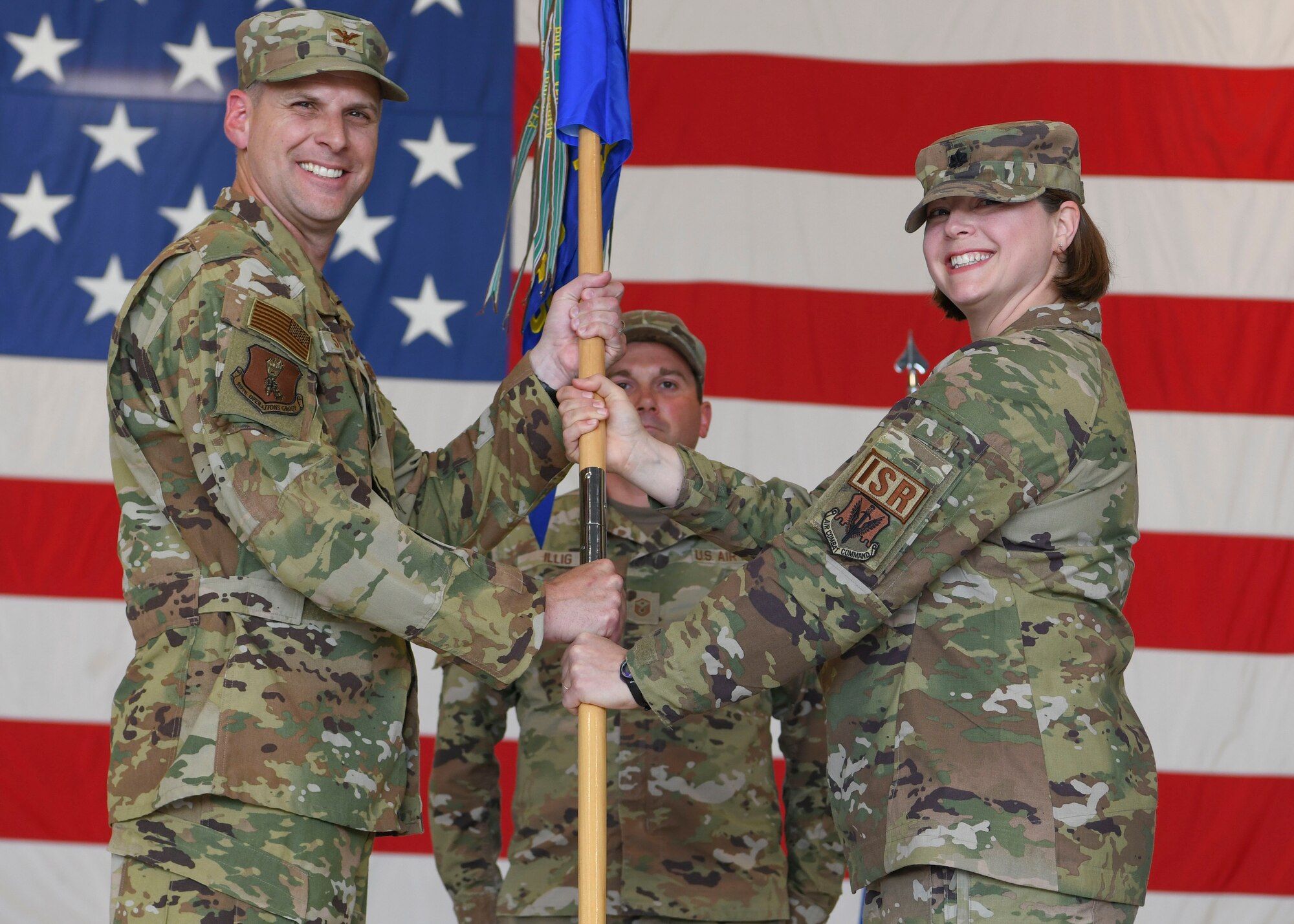 A man  and a woman in green uniforms hold on to a flag.
