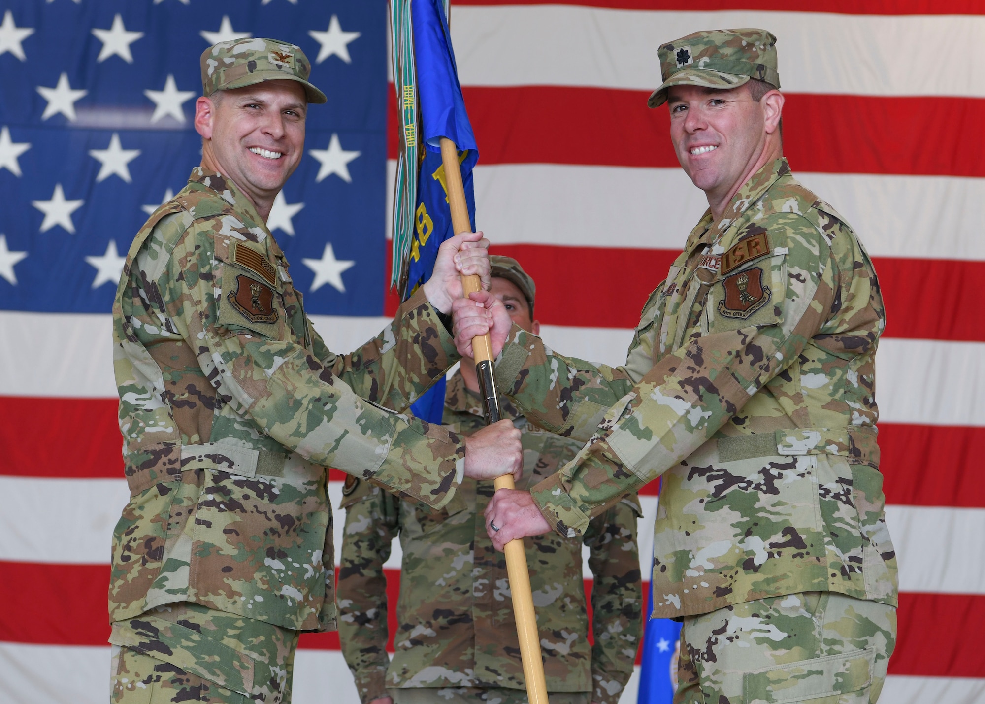 Two men in green uniforms hold a flag.