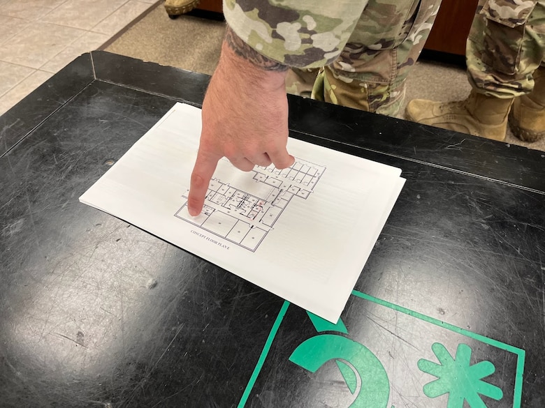 A man's hand is pointing to a piece of paper with a building design on it on top of a black table.