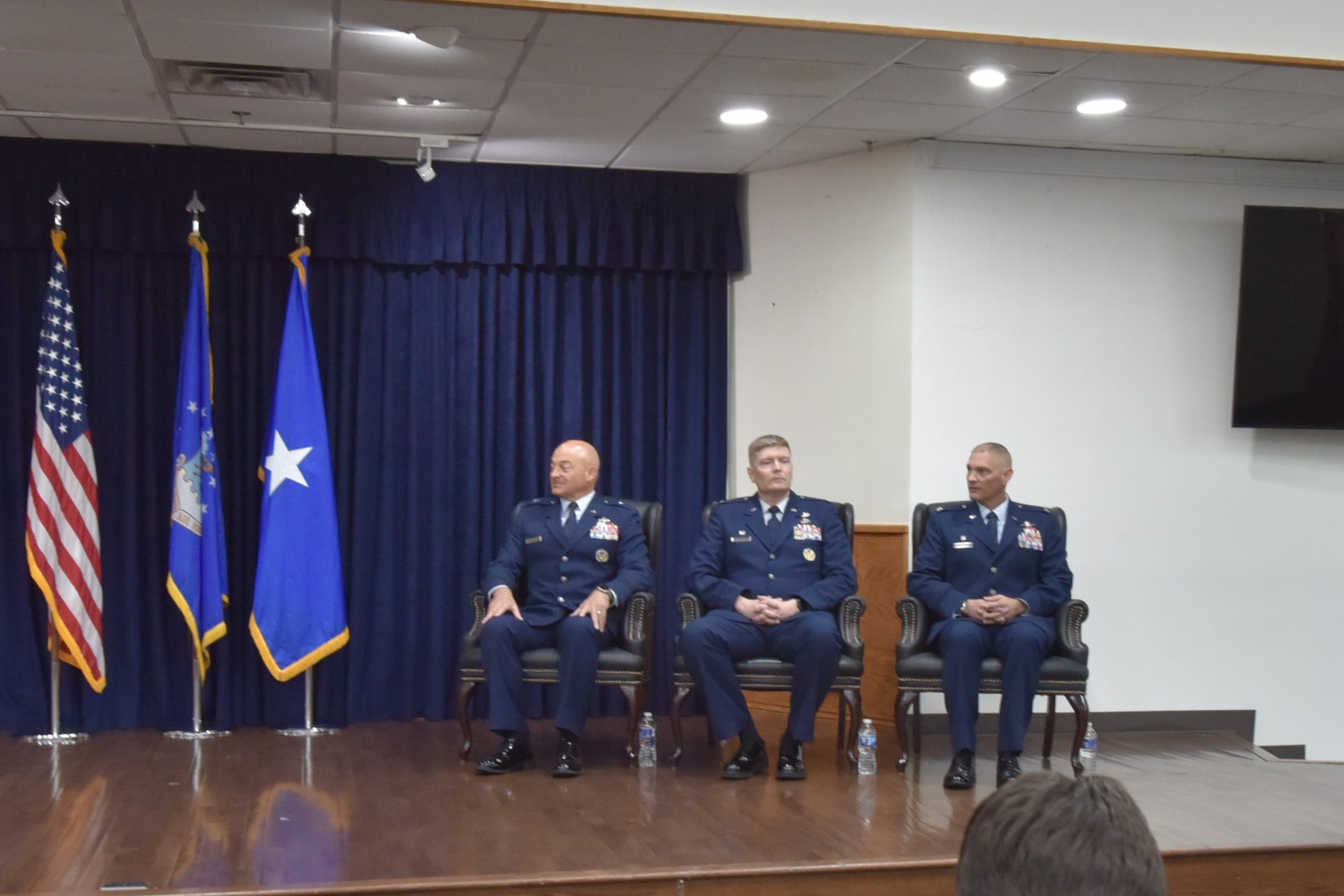 Three men in Air Force Uniforms sit in chairs on a stage.