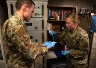 Two Air Force bioenvironmental engineers standing in a missile launch control center place a drop of liquid onto a gauze pad.
