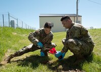 Air Force bioenvironmental engineers on a grass covered hill use a trowel to place a soil sample into a glass jar.