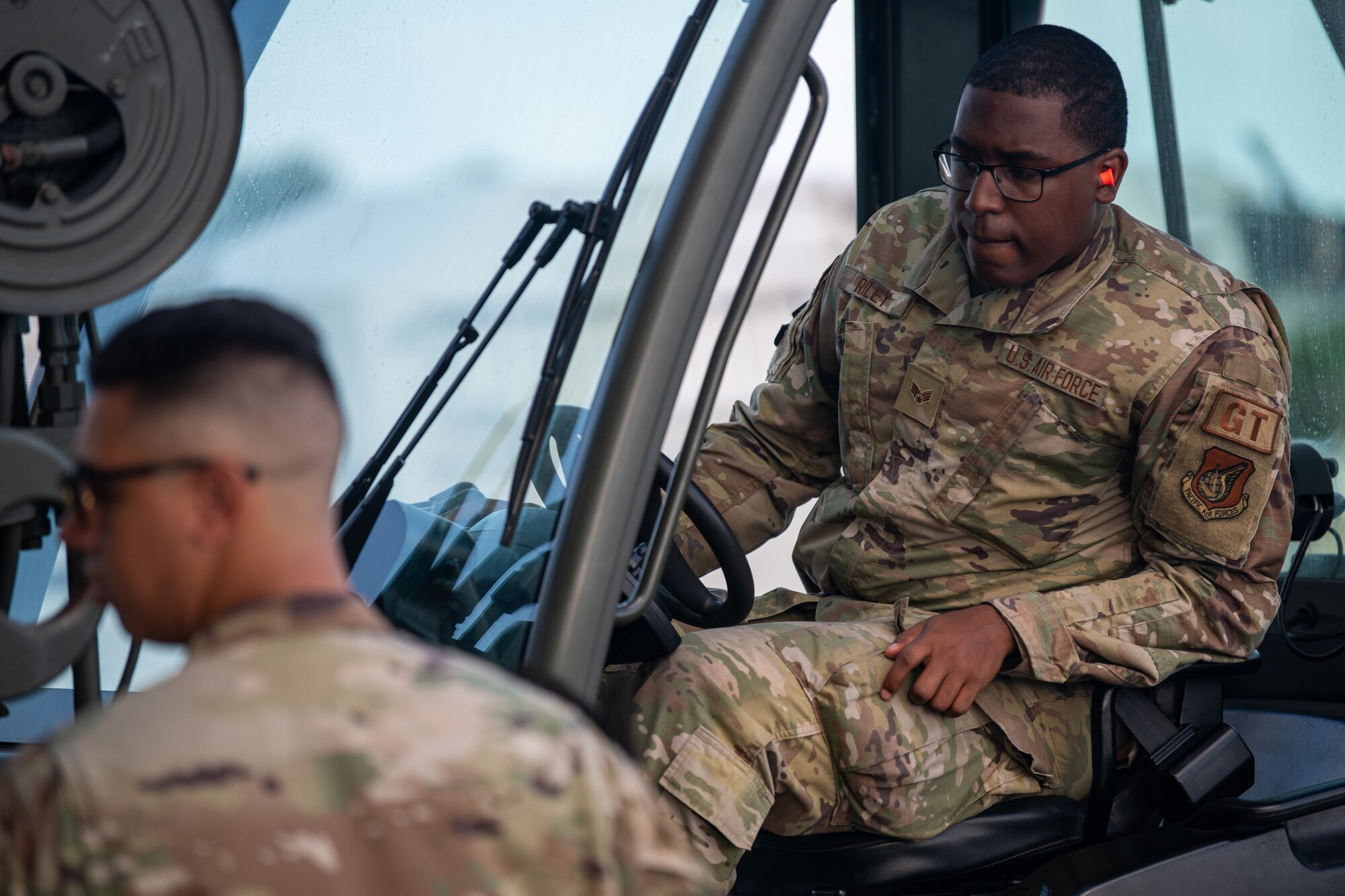 A man operates a vehicle while another man looks left.