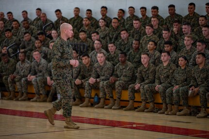 A man in military uniform speaks to a crowd of troops.