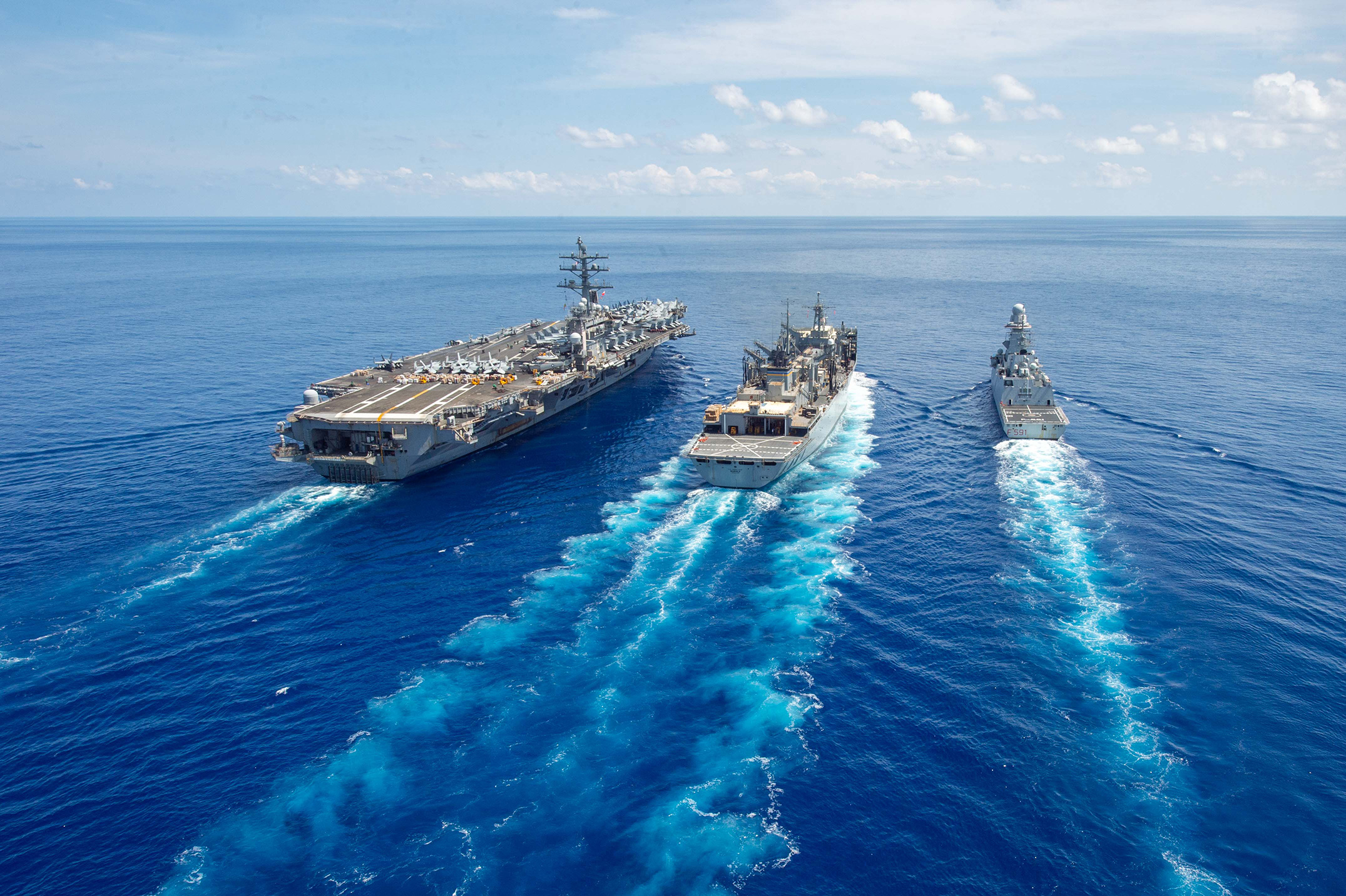 Three ships sail together in open water.