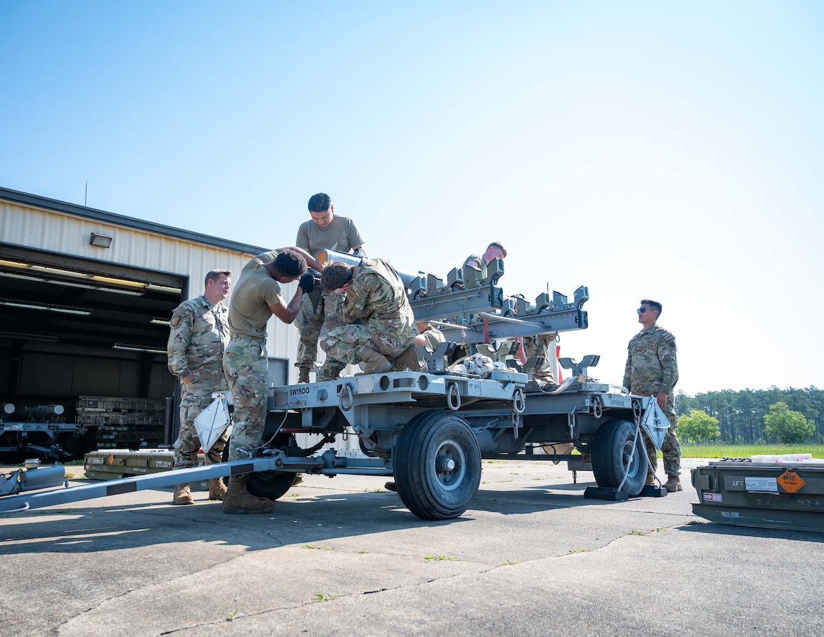 A load crew lifts munitions onto a transportation unit.