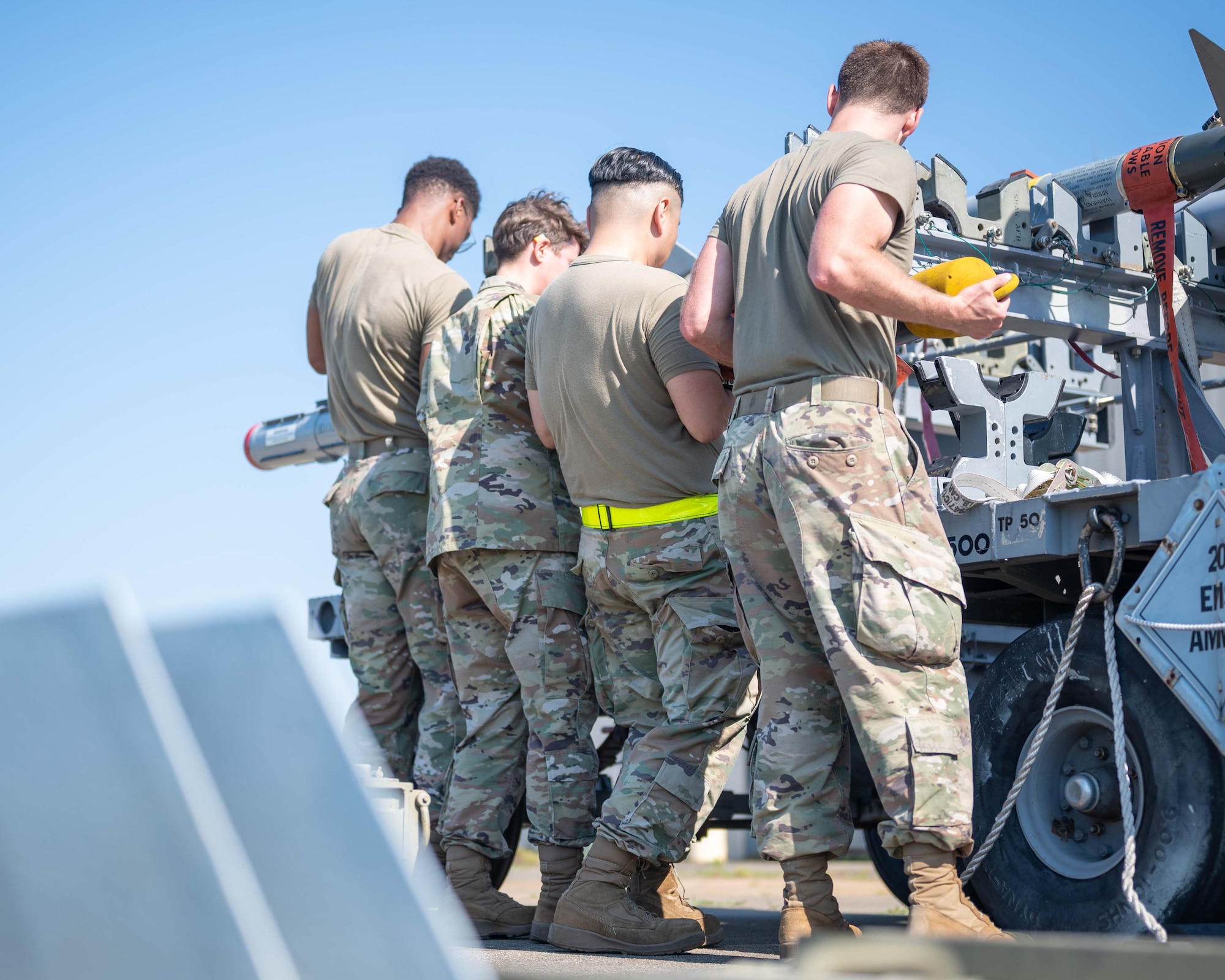 Four Airmen perform a team lift on a missile onto a transportation unit.