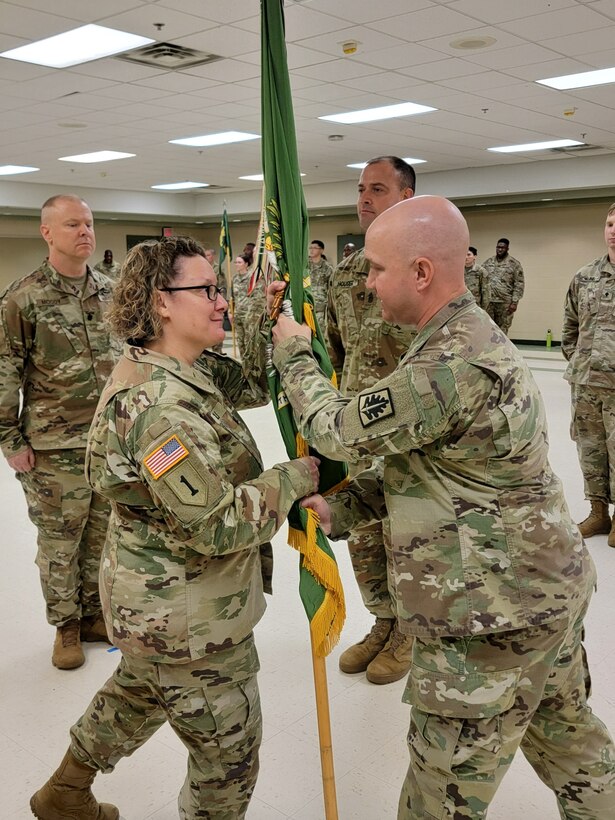 A Soldier passes the military unit colors to another Soldier in a formation.