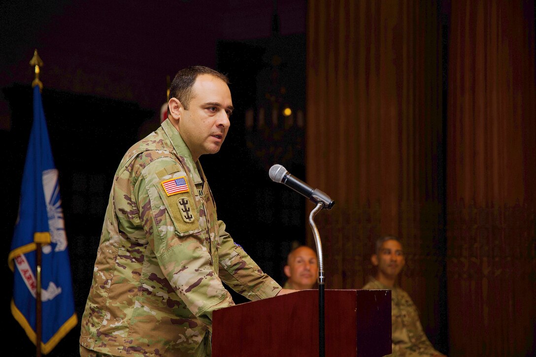 Photo shows a military officer making remarks at a podium.