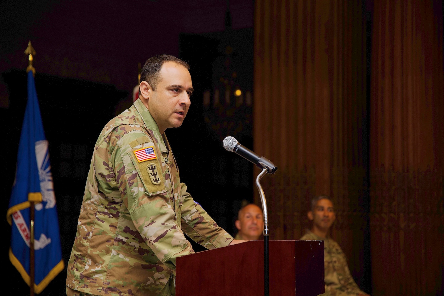 Photo shows a military officer making remarks at a podium.