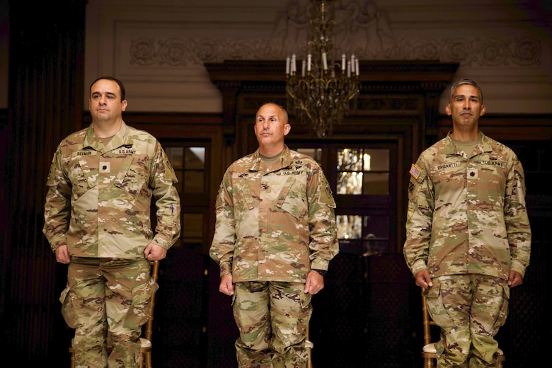 Photo shows three military officers standing at attention during a ceremony