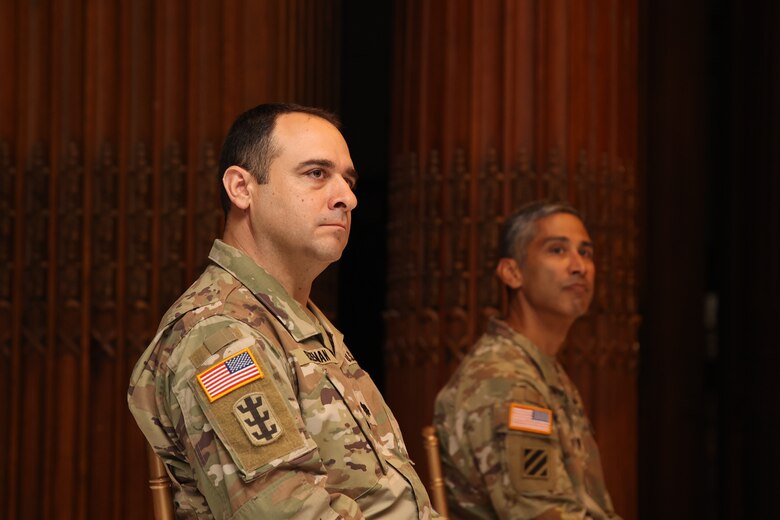 Photo shows two military officers listening to remarks during a ceremony