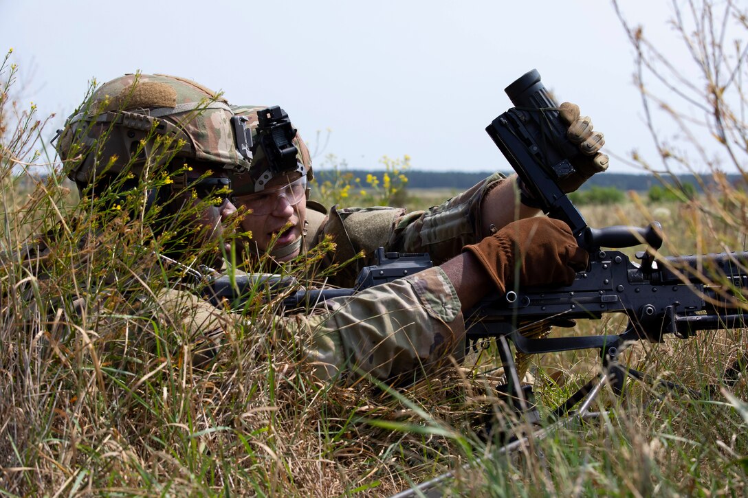 Two soldiers load a belt-fed light machine gun.