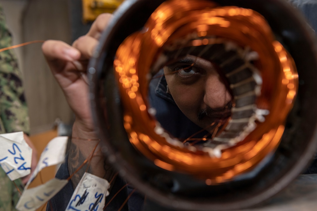 A sailor looks closely at the inside of a motor.