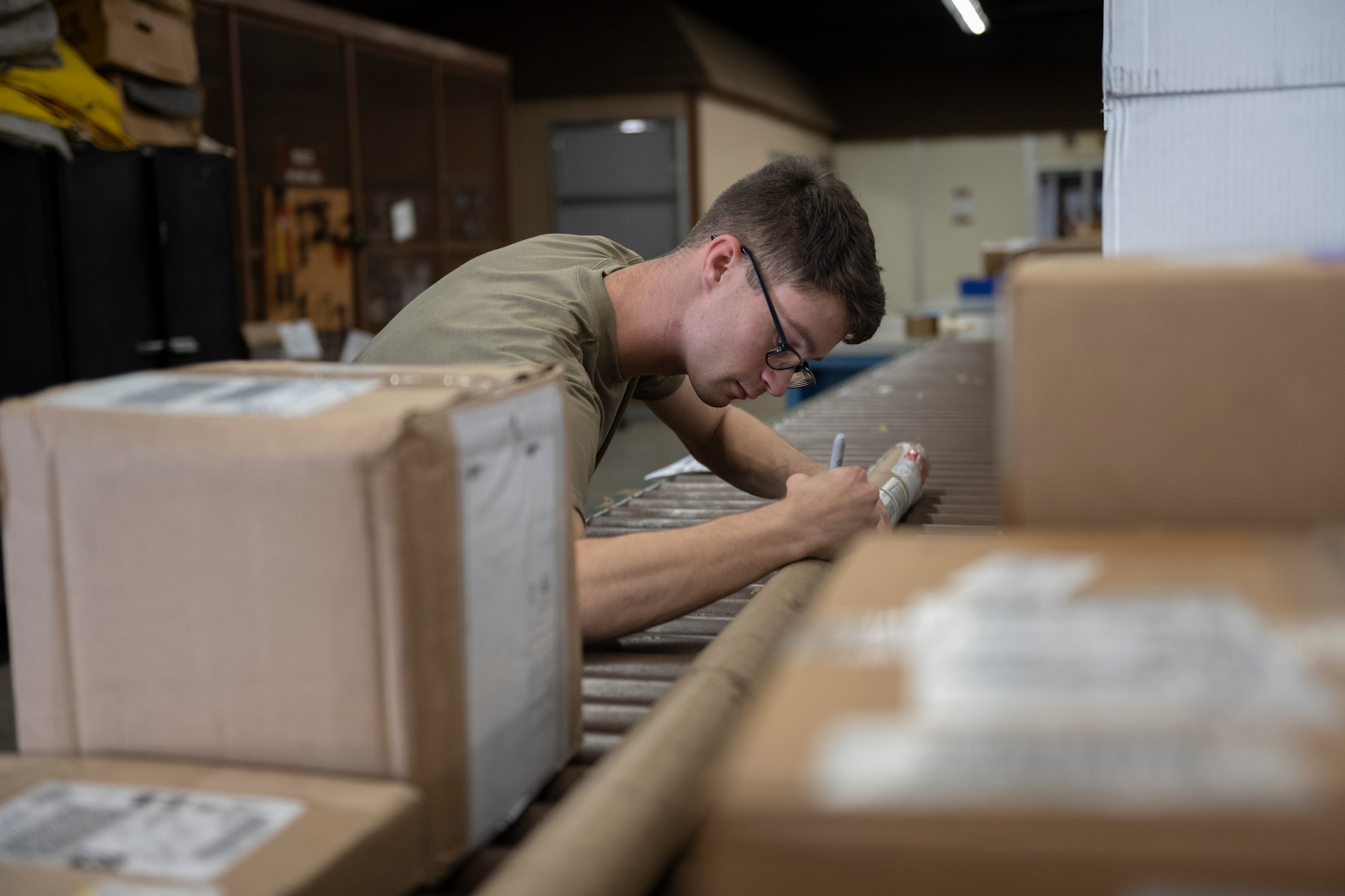 A photo of a person holding a cylindrical package steady to write on it with a black marker.