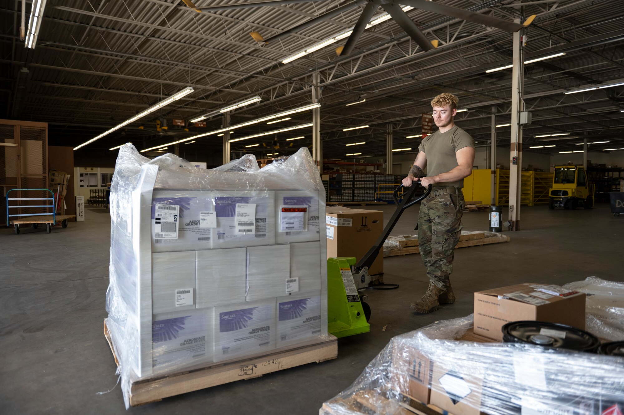 A photo of a person pulling a crate with boxes on it that are wrapped in clear plastic film.